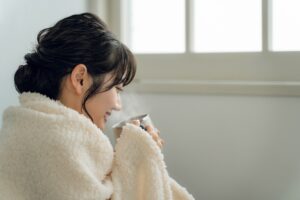 女性が温かい飲み物を手に座りながら暖を取る様子