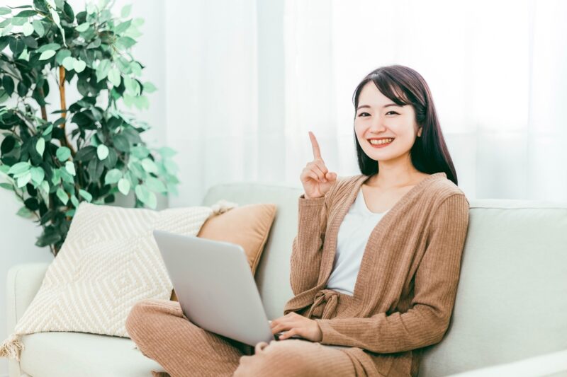 ソファーに座りパソコンを操作している笑顔の女性
